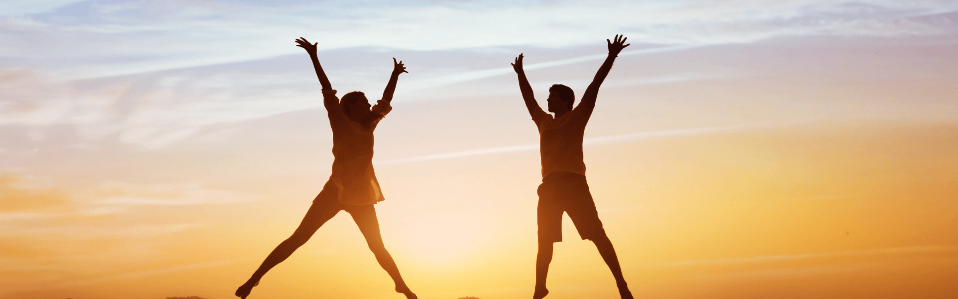 Silhouetted figures jump joyfully with arms raised against a vibrant sunset sky, suggesting celebration and freedom in an open outdoor environment.