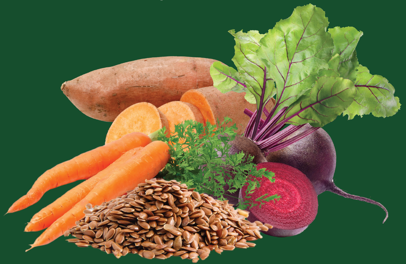 A variety of raw vegetables and seeds includes whole and sliced sweet potatoes, carrots, beets with leaves, and a pile of flaxseeds, arranged on a solid green background.