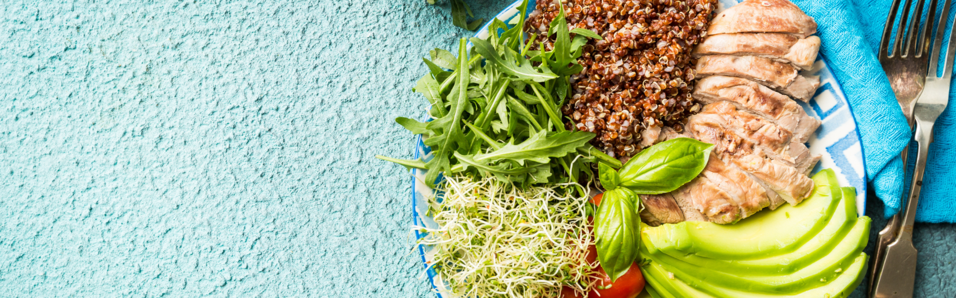 A vibrant plate contains sliced grilled chicken, quinoa, arugula, avocado, and sprouts, set against a textured light blue background with a fork and knife on a blue napkin.