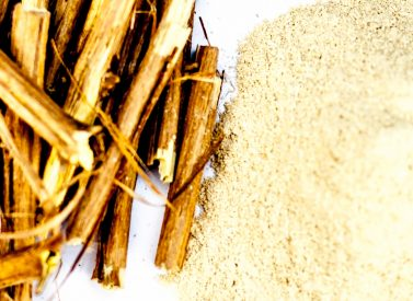 Bundled wooden sticks lie next to a small pile of beige powder on a smooth, white surface.