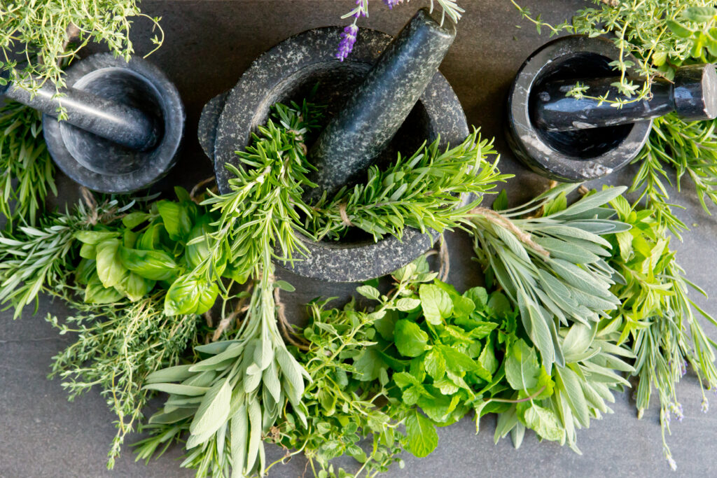Bird's eye view shot of three mortar and pestles on a table, with an abundance of scattered herbs in the mortar and on the table.